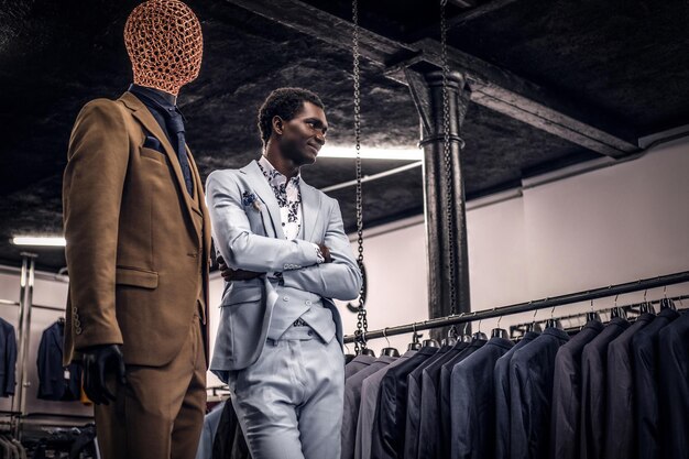 Un apuesto hombre afroamericano bien vestido posando con los brazos cruzados en una clásica tienda de ropa masculina.