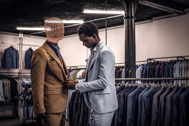 Un apuesto hombre afroamericano elegantemente vestido que trabaja en una tienda clásica de ropa de hombre.