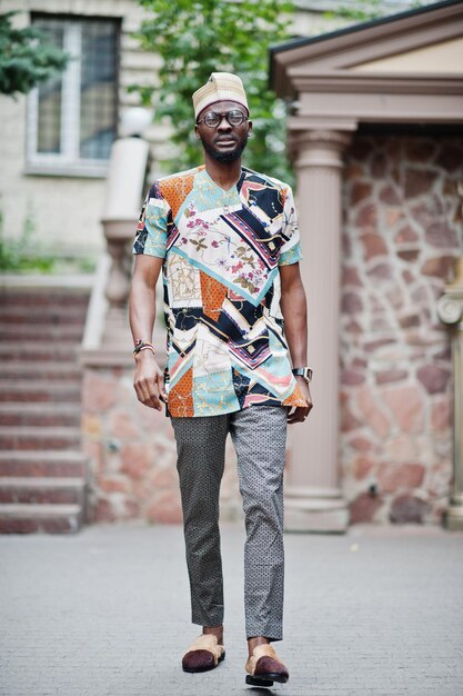 Apuesto hombre afroamericano con gorra de ropa tradicional y anteojos en la ciudad moderna