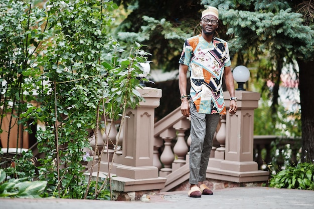 Apuesto hombre afroamericano con gorra de ropa tradicional y anteojos en la ciudad moderna