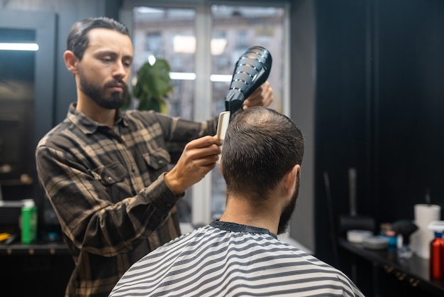 Un apuesto hombre barbudo se está peinando con un peluquero en la barbería