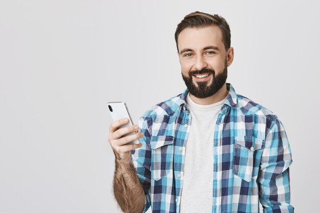 Apuesto hombre barbudo sonriente haciendo llamada telefónica