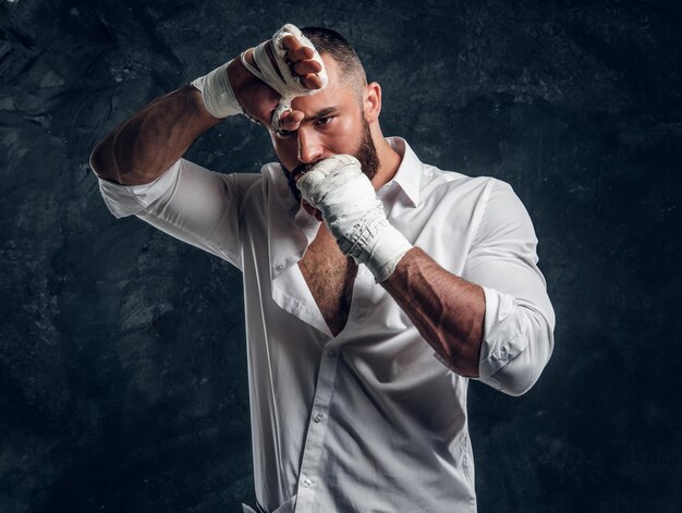 Un apuesto hombre brutal con guantes protectores de boxeo está mirando el protector bucal mientras posa para el fotógrafo.