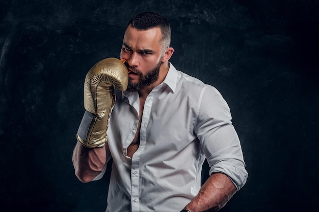 Un apuesto hombre brutal con guantes protectores de boxeo está mirando el protector bucal mientras posa para el fotógrafo.