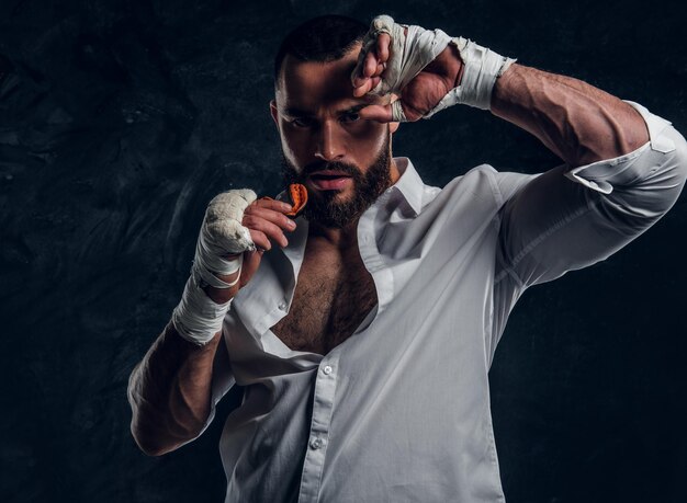 Un apuesto hombre brutal con guantes protectores de boxeo está mirando el protector bucal mientras posa para el fotógrafo.