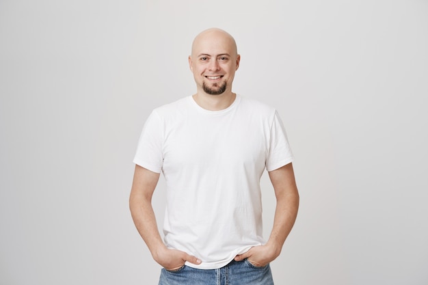 Apuesto hombre de mediana edad calvo sonriente con barba vistiendo camiseta blanca casual