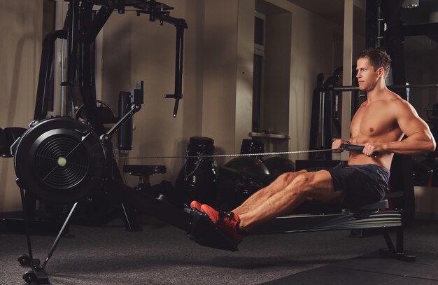 Un apuesto hombre musculoso haciendo ejercicio en la máquina de remo.