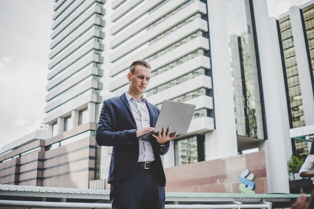 Apuesto hombre de negocios de camino a la oficina con la computadora portátil en la mano.