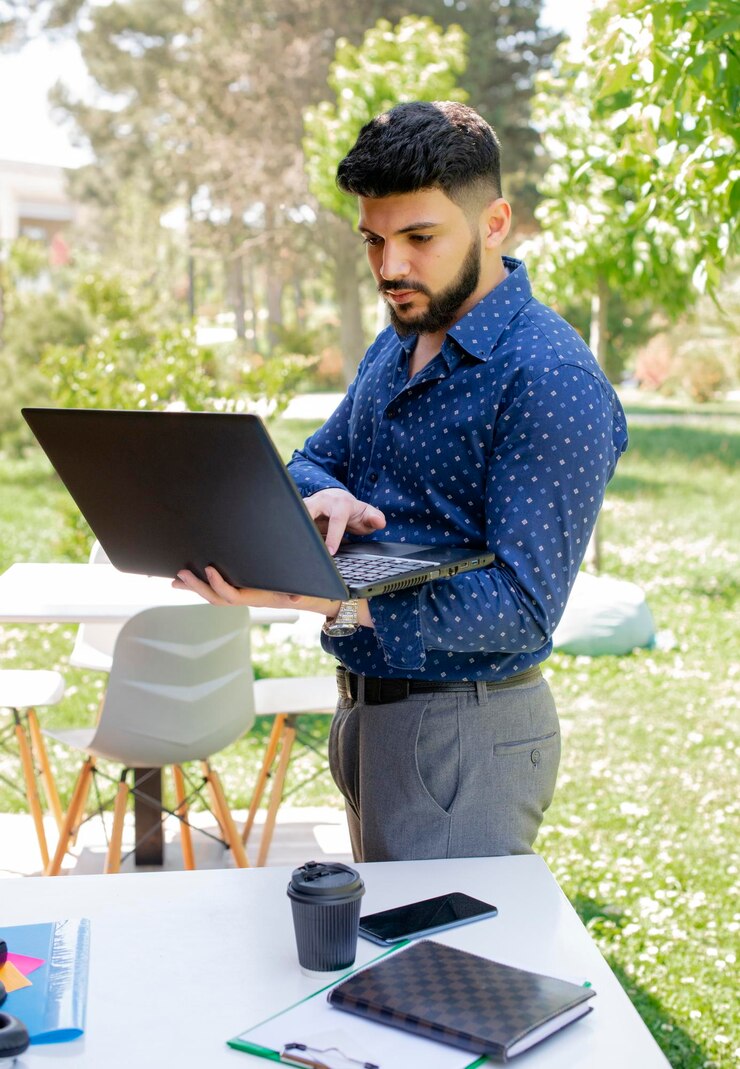 Foto gratuito apuesto hombre de negocios caucásico escribiendo en la computadora portátil al aire libre