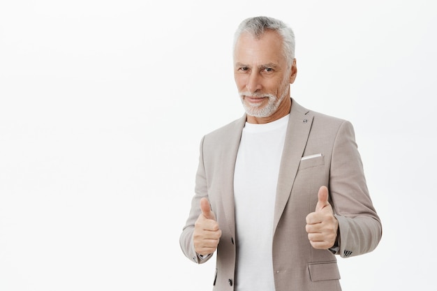 Apuesto hombre de negocios exitoso sonriendo, mostrando el pulgar hacia arriba en señal de aprobación