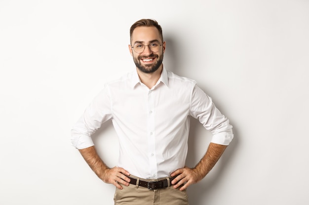 Apuesto hombre de negocios con gafas mirando satisfecho, sonriendo y tomados de la mano en la cintura, de pie