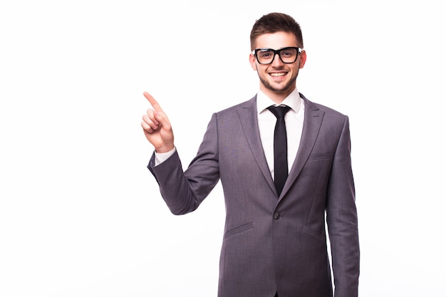 Apuesto hombre de negocios con gafas de pie con la mano en el bolsillo de una manera y apuntando a un lado feliz sobre fondo blanco de estudio