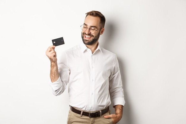 Apuesto hombre de negocios mostrando su tarjeta de crédito, mirando satisfecho, de pie