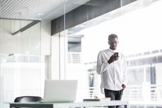 Apuesto hombre de negocios en ropa casual y anteojos es usar en el teléfono móvil en la oficina