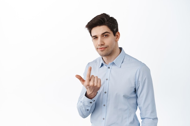 Apuesto hombre de negocios, señuelo de hombre corporativo, dígale que se acerque, haga señas para que se acerque a él, con aspecto serio, de pie sobre una pared blanca