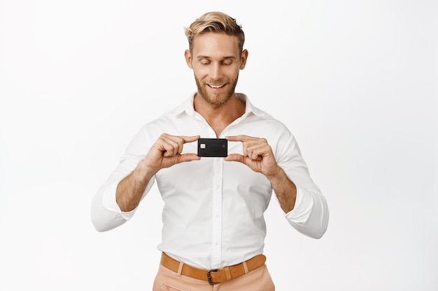 Apuesto hombre de negocios sonriente que muestra la tarjeta de crédito que demuestra el espacio de copia de fondo blanco del producto bancario