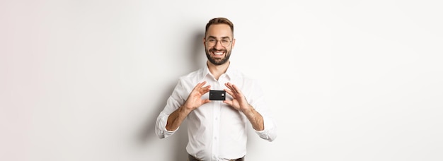 Apuesto hombre de negocios sosteniendo una tarjeta sonriendo satisfecho de pie sobre fondo blanco.