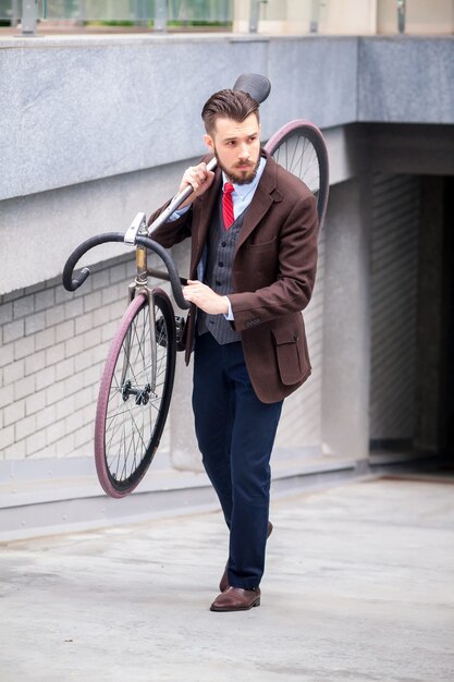 Apuesto hombre de negocios con su bicicleta por las calles de la ciudad. El concepto del estilo de vida moderno de los hombres jóvenes.