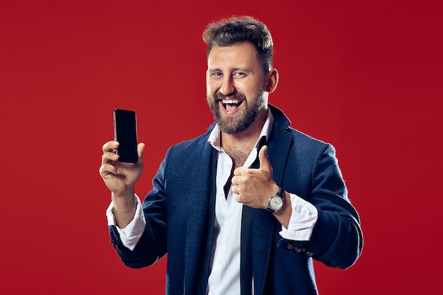 Apuesto hombre de negocios con teléfono móvil. Hombre de negocios feliz de pie aislado sobre fondo rojo de estudio. Hermoso retrato masculino de medio cuerpo