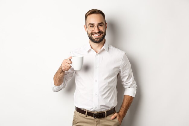 Apuesto hombre de negocios tomando café y sonriendo, de pie