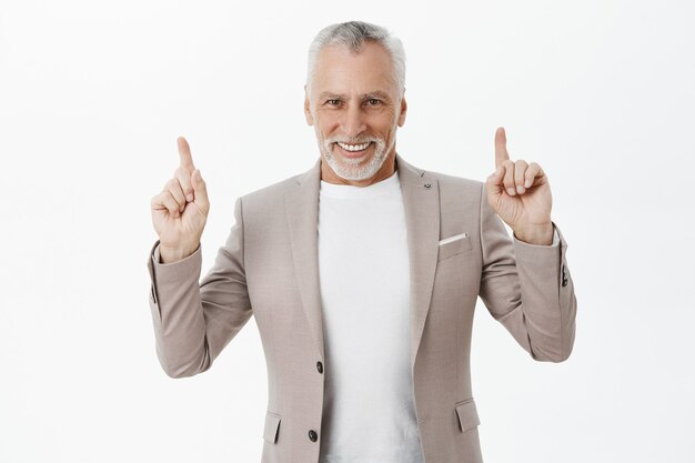 Apuesto hombre de negocios en traje apuntando con el dedo hacia arriba y sonriendo complacido