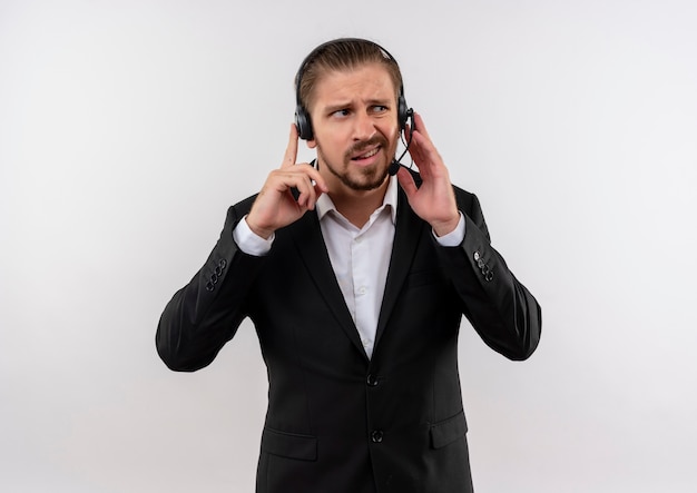 Apuesto hombre de negocios en traje y auriculares con un micrófono escuchando a un cliente que parece confundido de pie sobre fondo blanco.