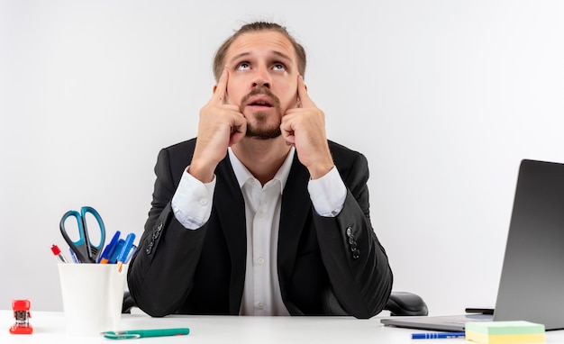 Foto gratuita apuesto hombre de negocios en traje buscando cansado y aburrido sentado a la mesa en offise sobre fondo blanco.