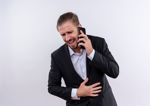 Apuesto hombre de negocios vestido con traje hablando por teléfono móvil decepcionado de pie sobre fondo blanco.