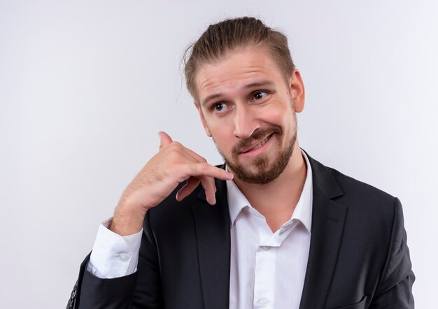 Apuesto hombre de negocios vestido con traje mirando a un lado haciendo gesto de llamarme de pie sobre fondo blanco.