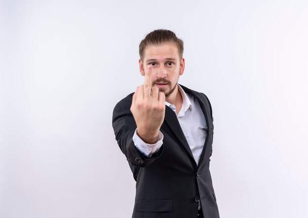 Apuesto hombre de negocios vestido con traje mostrando el dedo medio de pie sobre fondo blanco.