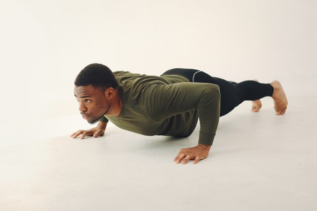 Apuesto hombre negro haciendo yoga en una pared blanca