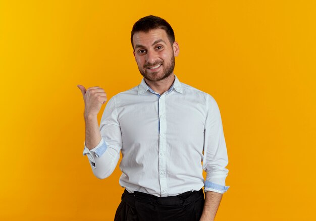 Apuesto hombre sonriente apunta al lado aislado en la pared naranja