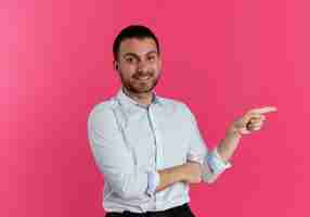 Foto gratuita apuesto hombre sonriente apunta al lado aislado en la pared rosa