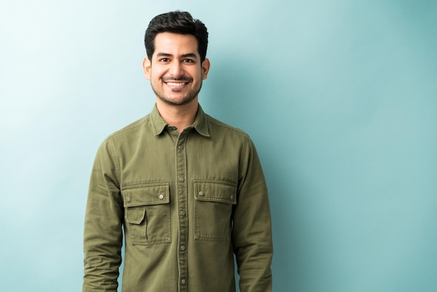 Apuesto hombre sonriente con camisa verde de pie contra el fondo azul.