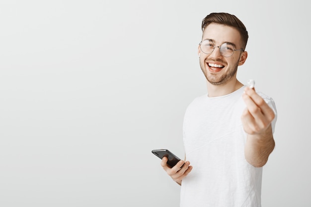 Apuesto hombre sonriente con gafas sugiere su auricular para escuchar música juntos, dándote auriculares