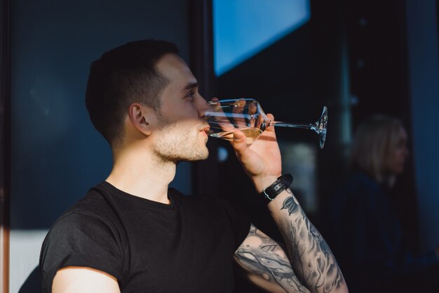 Apuesto hombre tatuado en una terraza de verano en un café de la ciudad está bebiendo vino. Calle Cafe.