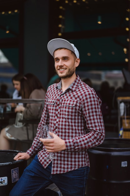 Apuesto hombre tatuado en una terraza de verano en un café de la ciudad está bebiendo vino. Calle Cafe.