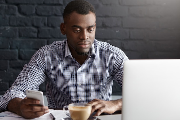 Apuesto joven africano en camisa formal navegando por internet en el teléfono móvil