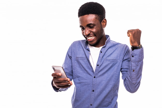 Apuesto joven africano con teléfono móvil y gesticulando mientras está de pie contra la pared gris