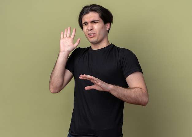 Apuesto joven aprensivo con camiseta negra aislada en la pared verde oliva