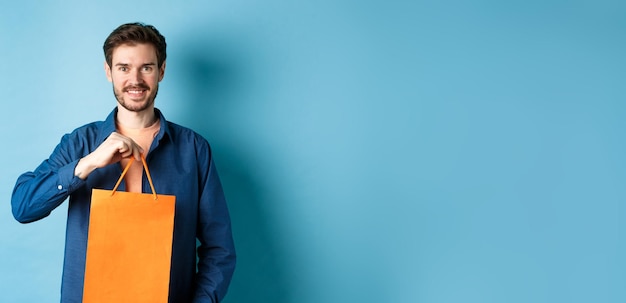 Foto gratuita apuesto joven con barba sonriendo y mostrando bolsa de compras comprando algo en la tienda de pie en