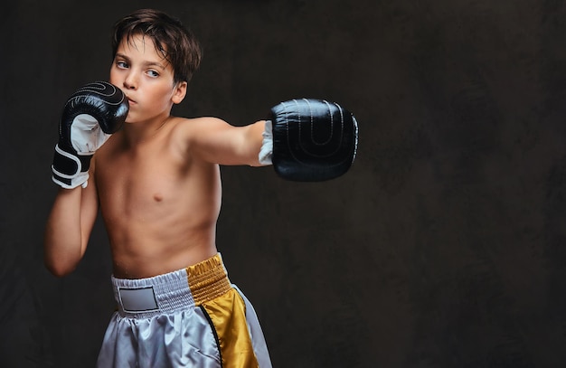 Apuesto joven boxeador sin camisa durante los ejercicios de boxeo, centrado en el proceso con un facial concentrado serio.