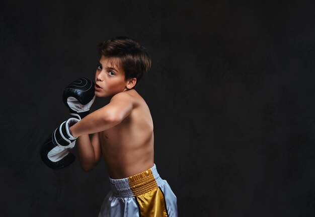 Apuesto joven boxeador sin camisa durante los ejercicios de boxeo, centrado en el proceso con un facial concentrado serio.