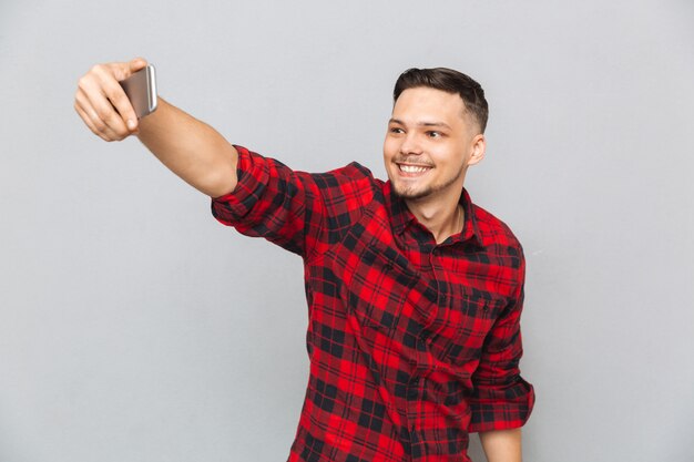 Apuesto joven en camisa a cuadros haciendo selfie