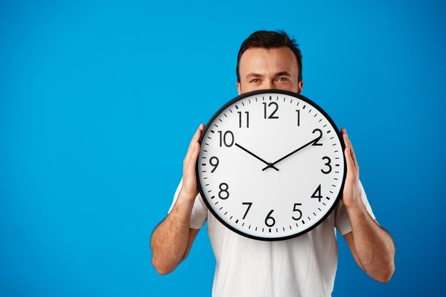 Apuesto joven en camiseta blanca posando con reloj sobre fondo azul.