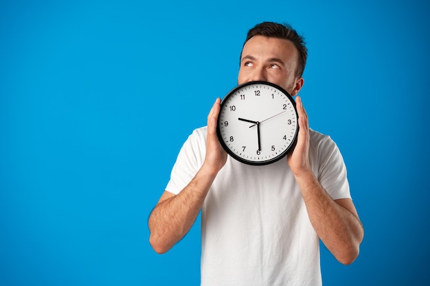 Apuesto joven en camiseta blanca posando con reloj sobre fondo azul.