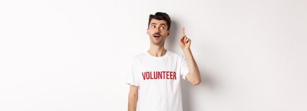 Foto gratuita apuesto joven en camiseta voluntaria que tiene una idea levantando el dedo y diciendo sugerencia bac blanco