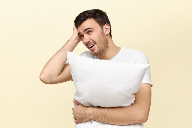 Apuesto joven cansado con almohada blanca