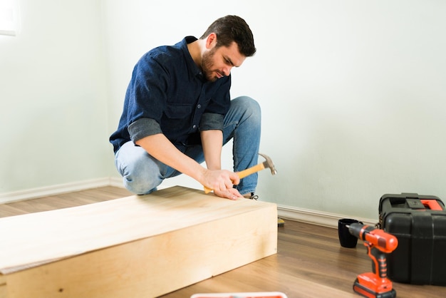 Apuesto joven construyéndose un nuevo estante de madera y haciendo algunas renovaciones caseras de bricolaje