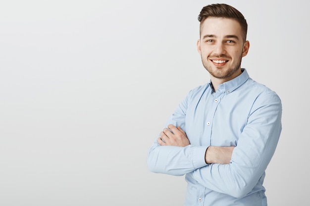 Apuesto joven empresario con brazos cruzados sonriendo confiado